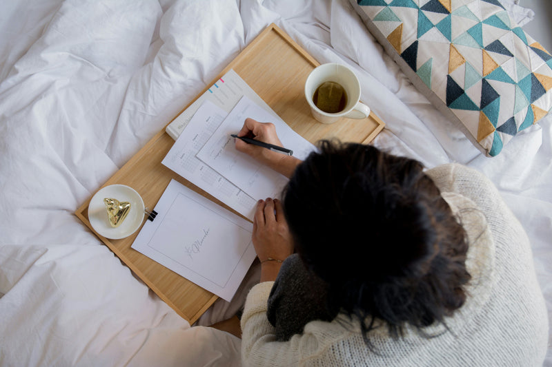 Woman writing her daily plans in bed with a cup of coffee using planner pages from The Planner Shop